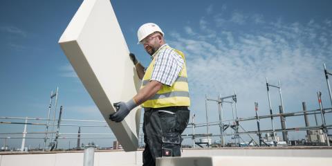 Construction worker on a building site holding a thick, rigid panel of PU insulation.