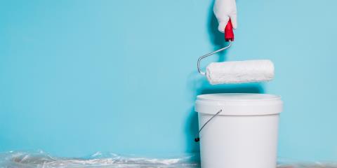 Image of paint can and man holding paint roller in front of blue wall.