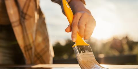 Person in lumberjack shirt painting outside with a small yellow brush